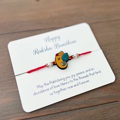 a red string bracelet with a happy radha bandon on it sitting on top of a wooden table