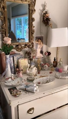 there is a dresser that has many items on it and a mirror above it with flowers