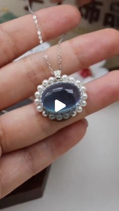 a person holding a necklace with a blue stone in it's center and pearls around the edges