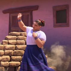 a woman standing in front of a pile of rocks with her hand up to the sky