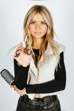 a woman holding scissors in her right hand and looking at the camera while wearing leather pants