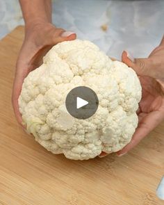 a person holding a piece of cauliflower on top of a wooden cutting board