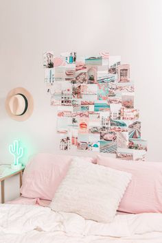 a white bed topped with pink pillows next to a wall covered in pictures and lights