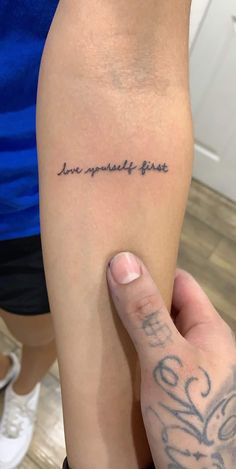 a person with a tattoo on their arm and the words love yourself first written in cursive writing