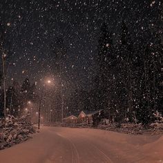 a snow covered road at night with street lights in the distance and trees on either side