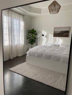 a large mirror reflecting a bed in a room with white walls and wood flooring