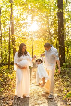 a pregnant woman and her husband walk down a path in the woods with their child