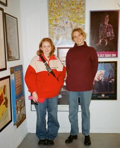 two women standing next to each other in front of pictures and posters on the wall