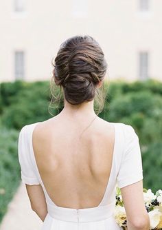 the back of a bride's dress with flowers in her hair and holding a bouquet