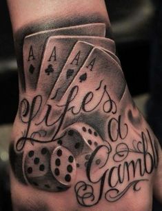 a man's hand with some tattoos on it and playing cards in the middle