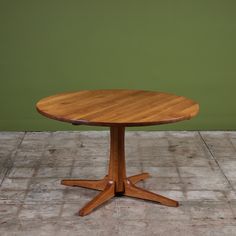 a wooden table sitting on top of a cement floor next to a green wall and white tile