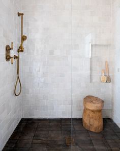 a white tiled bathroom with a wooden stool and shower head