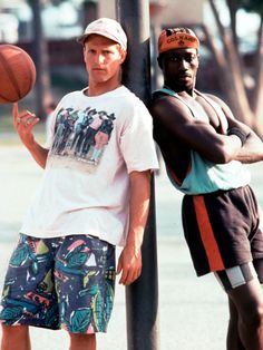 two young men standing next to each other near a pole with a basketball on it