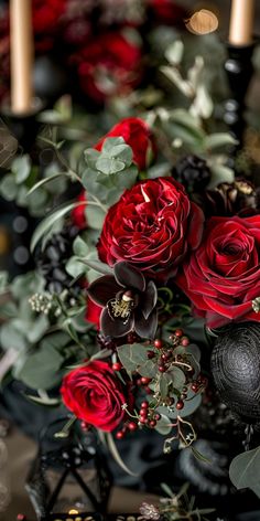 a bouquet of red roses and greenery with candles in the background