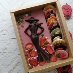 a box filled with assorted donuts and a woman figure in the middle surrounded by fruit