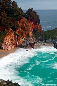 an ocean view with waves crashing on the shore and trees lining the shoreline near the water's edge