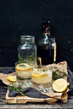 two glasses filled with lemonade sitting on top of a wooden table next to bottles