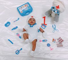 a baby laying on top of a white sheet next to toys and other items that include an infant's first toothbrush