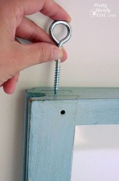 a person is holding a screw in front of a blue frame with a mirror behind it