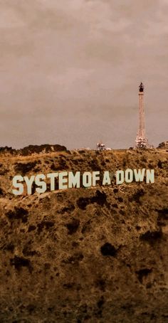 there is a sign that says system of a down on top of a hill with a lighthouse in the background