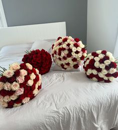 three large bouquets of roses on a bed with white sheets and pillows in the background