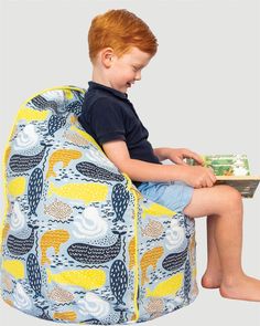 a young boy sitting in a bean bag chair with a book on it's lap