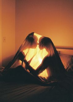 two people are sitting on a bed under a sheered sheet with the light shining through them