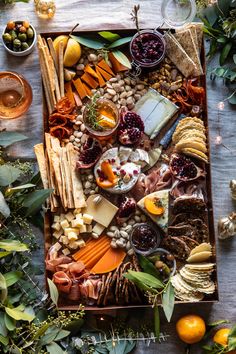 an assortment of cheeses, crackers and fruit on a tray surrounded by greenery