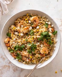 a white bowl filled with rice and shrimp next to a fork on top of a table