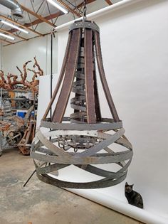 a cat is sitting on the floor next to a large metal sculpture in a warehouse