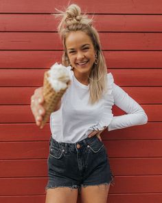 a woman holding an ice cream cone in front of a red wall with her hands behind her back