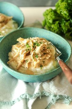 two blue bowls filled with mashed potatoes covered in chicken and garnished with parsley