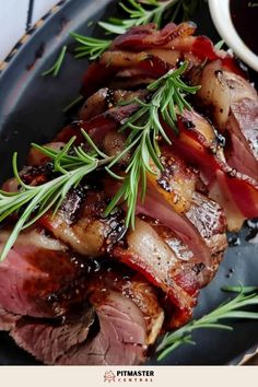 sliced meat on a plate with sauce and rosemary sprigs next to the dish