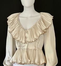 STUNNING vintage C1970s high end, off white or ivory sumptuous long sleeve silk blouse by Partique, featuring a lavish V neck collar with pleated ruffles fully edged in gold trim, a peplum hem, also with pleated ruffles fully edged in gold trim, and a three button front closure.  Channeling Old Hollywood elegance and glamour, this rare beauty is a guaranteed head turner! Approximate Measurements:      Chest: 38"; Shoulder: 16"; Waist: 27"; Length: 19 1/2"      Labeled a Size 6 Please Note:  Partique blouse shown with Apostrophe brown silk slacks and Albert Capraro gold silk slacks for illustration only; the slacks are not included in this listing but are available separately.  Likewise, the two belts shown with this blouse are for illustration only; they are not included in this listing bu White Leather Gloves, 1970s Blouse, Black Sequin Skirt, V Neck Collar, White Silk Blouse, Party Blouse, Gold Blouse, Silk Tulle, Ivory Silk