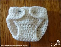 a white crocheted diaper with a button on the side sitting on a wooden floor