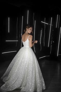 a woman wearing a white dress standing in front of a black wall with lights on it