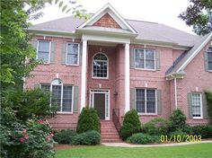 a red brick house with white trim and large front porch surrounded by greenery, shrubs and trees