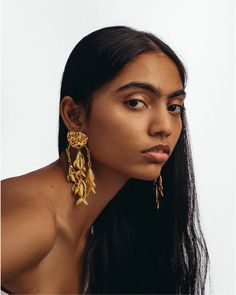 a woman with long black hair wearing gold earrings and looking off to the side, in front of a white background