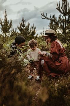 two women and a child are sitting in the middle of a field with pine trees