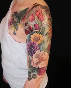 a woman's arm with flowers and birds on it, while she is wearing a white tank top