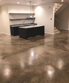 an empty kitchen and living room in a house with concrete floors, white walls and stairs