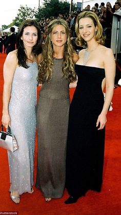 three women standing next to each other on a red carpet with people in the background