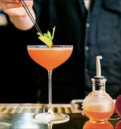 a person is holding a drink in front of a glass with a green garnish on it