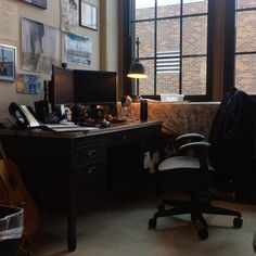 an office area with desk, chair and computer on the table in front of large windows