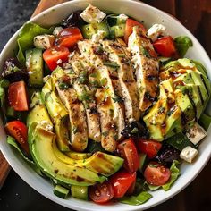 a salad with chicken, cucumber, tomatoes and olives in a white bowl