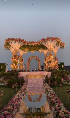 an outdoor wedding setup with flowers and greenery on the ground at dusk, lit up by lights