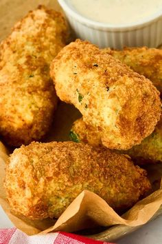 some fried food is in a paper basket with a dipping sauce on the side,