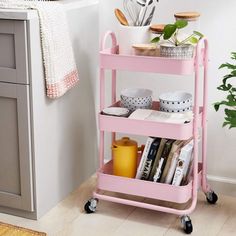 a pink rolling cart with magazines and other items on it in a white kitchen area