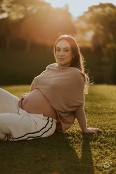 a pregnant woman laying on the grass at sunset