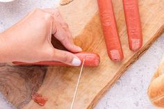 a person is cutting up some hot dogs on a cutting board with a pair of tongs